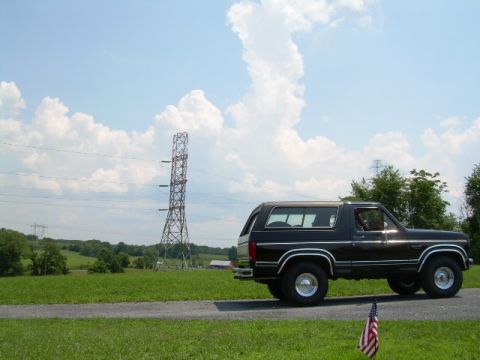 1984 Ford Bronco - A black SUV is parked on the side of a road with a large power transmission tower in the distance.
