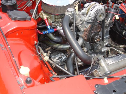 1986 Mazda RX-7 - The engine bay of a red vehicle features a rotary engine with various hoses and components visible.