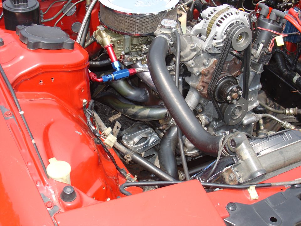 Close-up of a rotary engine in a red car's engine bay, showing the carburetor, alternator, and hoses