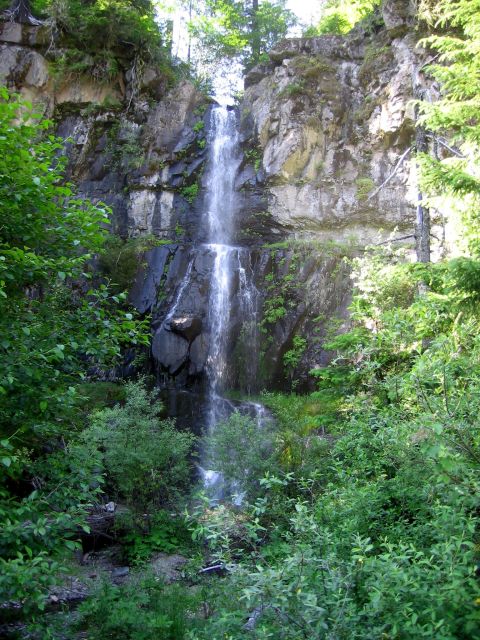 1979 Ford Bronco - A tall waterfall flows down a rocky cliff face, with lush green trees and bushes in the foreground.