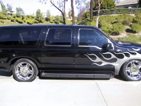 2001 Ford Excursion - Black 2001 Ford Excursion with custom flame graphics and chrome wheels is parked outside.