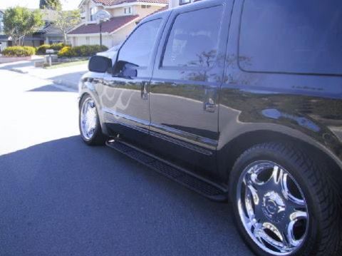 2001 Ford Excursion - A black 2001 Ford Excursion is parked on a residential street, showing its side profile and custom wheels.