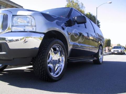 2001 Ford Excursion - A black SUV with flame decals and chrome wheels is parked on a street, with another car visible in the background.