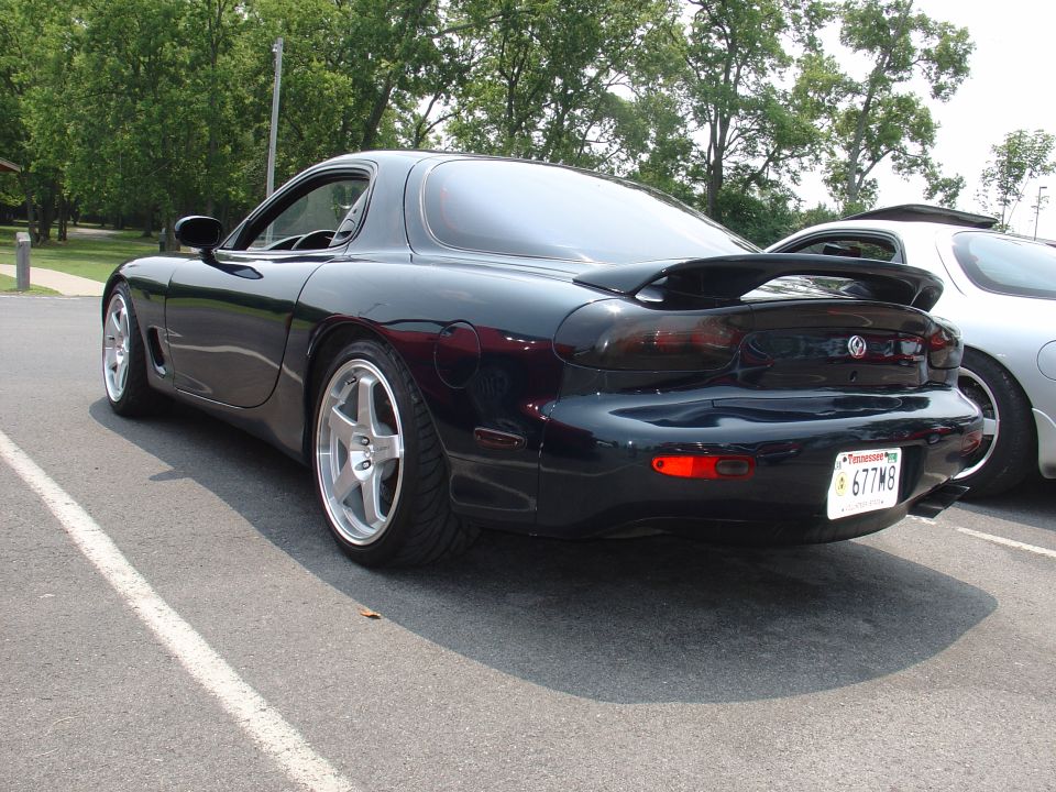 Dark blue Mazda RX-7 rear view with spoiler and aftermarket wheels. License plate 677M8