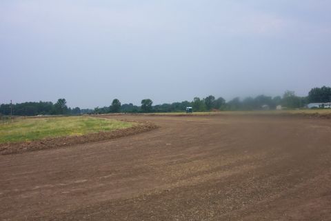 1978 Ford Bronco - A dirt track curves through a field under an overcast sky, with a distant white vehicle visible.