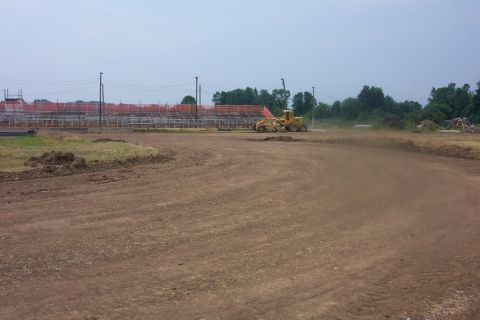 1978 Ford Bronco - A grader operates on a dirt track at a construction site with unfinished bleachers in the background.