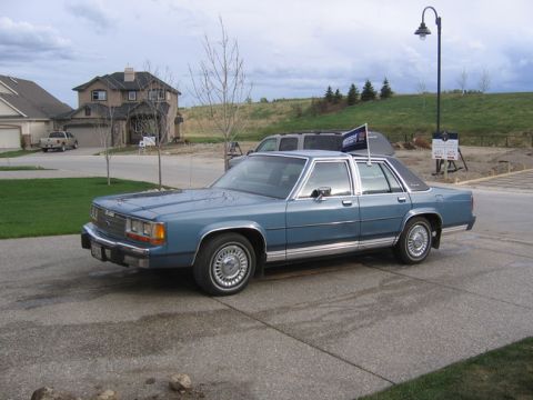 1988 Ford Crown Victoria LTD - This blue sedan has a distinctive body style from the 1980s, with chrome trim and a dark vinyl roof.