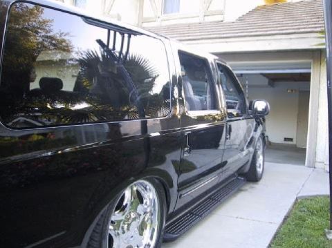 2001 Ford Excursion - Side view of a black SUV with custom chrome wheels and running boards parked in a driveway.