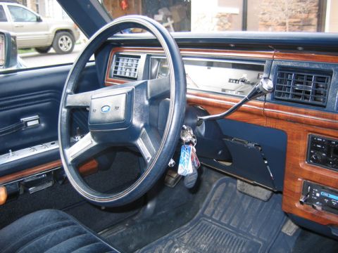 1988 Ford Crown Victoria LTD - The interior of a car shows a dashboard with wood grain accents and a Ford emblem on the steering wheel.