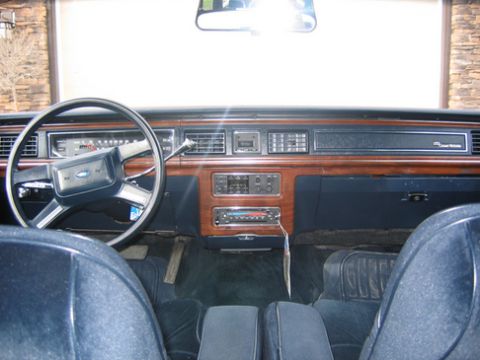 1988 Ford Crown Victoria LTD - The interior of a car features a wood-grain dashboard with a Ford steering wheel and blue seats.