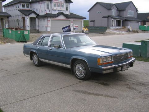 1988 Ford Crown Victoria LTD - A blue 1988 Ford Crown Victoria LTD is parked in front of a house under construction.