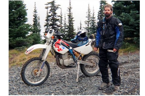 1997 BMW F650 - A man poses with his dirt bike in a wooded, gravelly area.