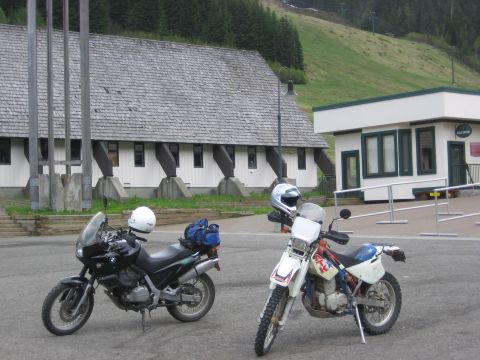 1997 BMW F650 - Two motorcycles are parked in front of a building with a wooden roof and a grassy hill behind them.