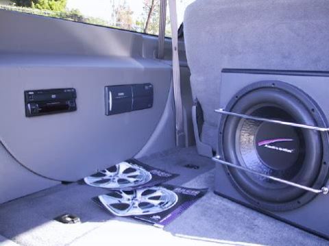 2001 Ford Excursion - The interior of a vehicle is shown, a large subwoofer, two car stereos mounted on the wall, and magazines displaying car wheels on the floo…