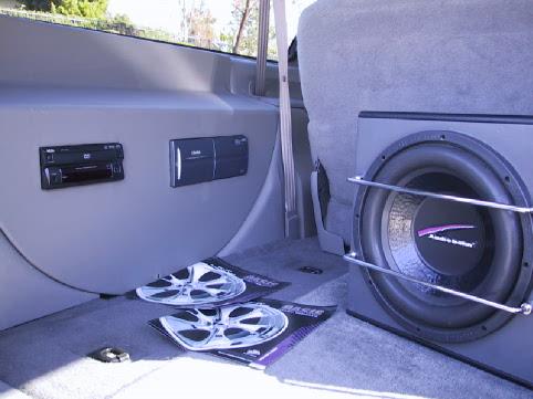 Cargo area audio install with subwoofer, head unit, and chrome wheels on floor