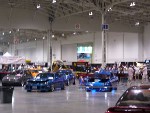 1995 Ford Taurus - Multiple custom cars are displayed indoors at a car show event.