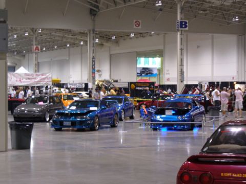 1995 Ford Taurus - Several modified cars are showcased indoors at an automotive event.