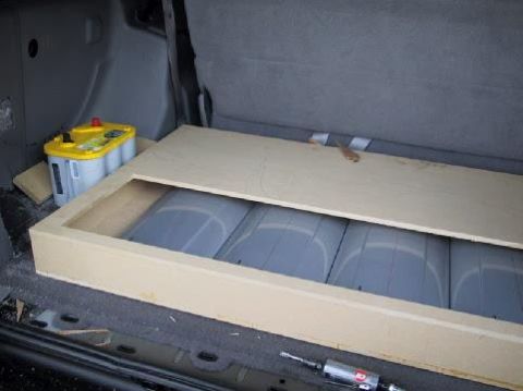 2001 Ford Excursion - Custom subwoofer box installed in the rear cargo area of a vehicle, next to a yellow Optima battery.