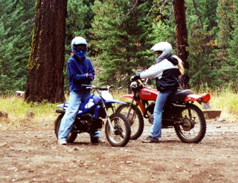 1997 BMW F650 - Two riders pose with their dirt bikes in a forest clearing.