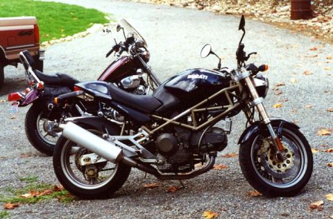 1997 BMW F650 - Two motorcycles and a pickup truck are parked on a gravel surface with fallen leaves.