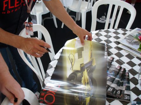 1995 Ford Taurus - Hands autographing a poster a racing car, with several brochures nearby.