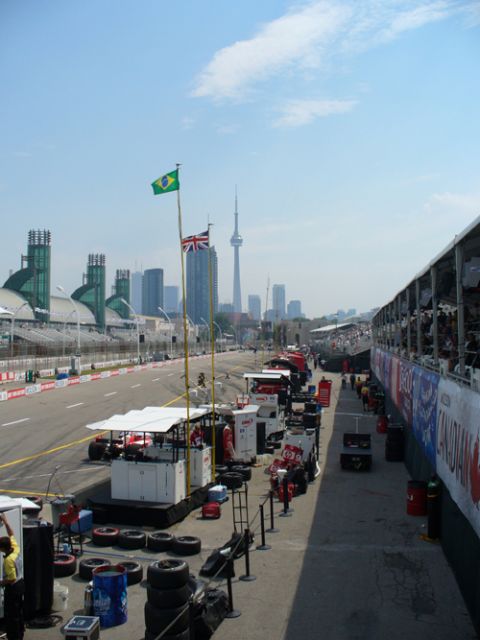 1995 Ford Taurus - A view of a race track pit lane with the Toronto skyline and CN Tower visible in the distance, under a bright sky.