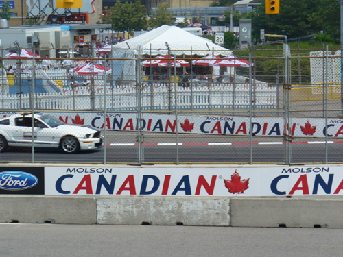 White Ford Mustang with racing stripes on a track, Molson Canadian banners in background