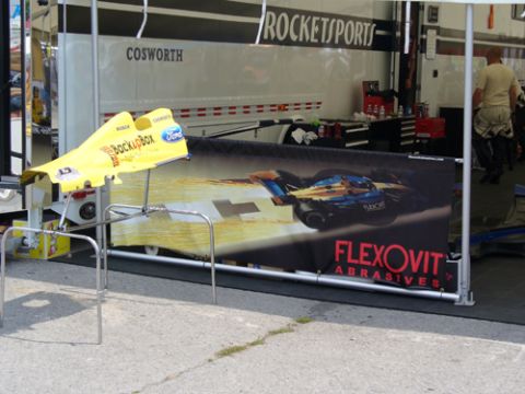 1995 Ford Taurus - A yellow race car aerodynamic part is displayed in front of a trailer and banner.