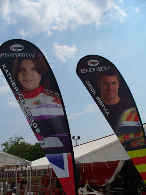 1995 Ford Taurus - Banners for Katherine Legge and Oriol Servia are displayed outdoors under a cloudy sky.