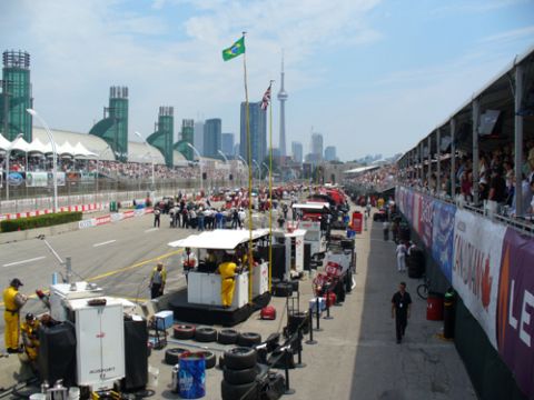 1995 Ford Taurus - Pit lane activity at a race track with a city skyline and grandstands full of spectators.