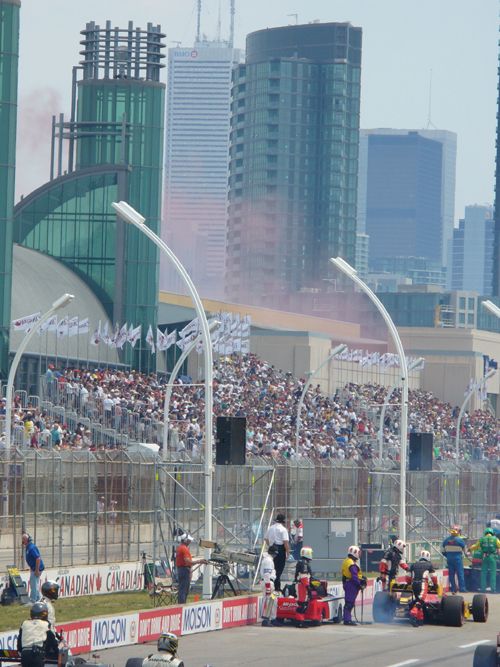 Race cars on track with crowd in stands and city skyline