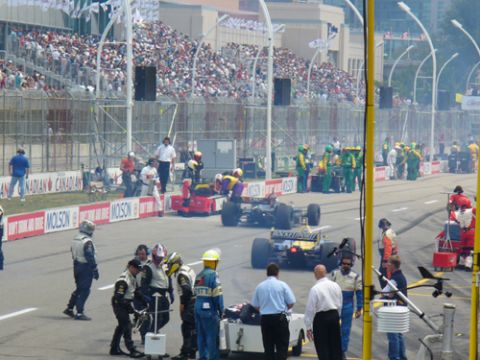 1995 Ford Taurus - Open-wheel cars on a street-circuit pit lane, pit crews in fire suits, Molson/Canadian banners and a packed grandstand behind.