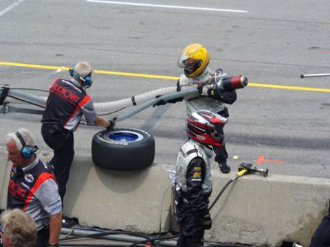 1995 Ford Taurus - Pit crew members prepare a tire during a race, with a hose and equipment visible.