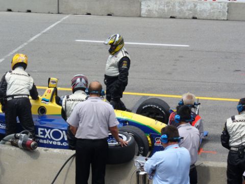 1995 Ford Taurus - A race car pit stop is underway with crew members attending to a yellow and blue vehicle on the track.
