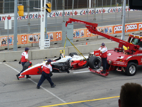 Red and white open-wheel race car being loaded onto a tow truck