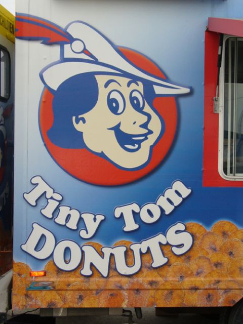 1995 Ford Taurus - A food truck displays "Tiny Tom Donuts" branding and a graphic of donuts on its side.