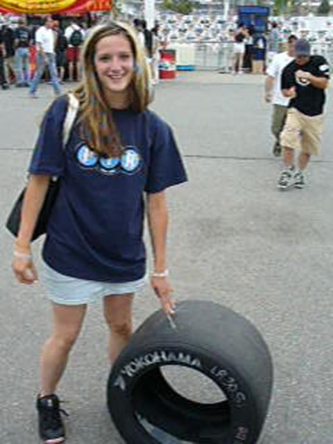 1995 Ford Taurus - A woman poses with a racing tire at an outdoor event with spectators and barriers visible.