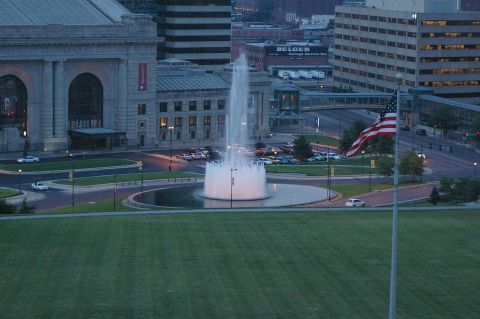 1998 Jeep TJ - Urban scene a fountain, flag, and vehicles, with a prominent building in the background.