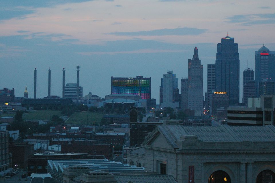 City skyline at dusk with smokestacks and a building lit with rainbow colors