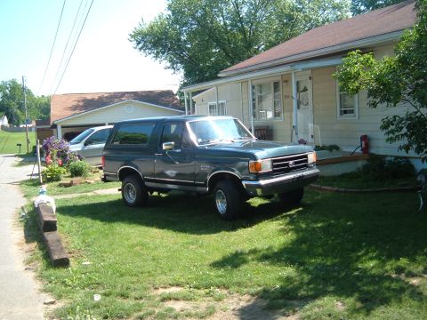 1988 Ford Bronco - A dark green Ford Bronco is parked on a grassy lawn in front of a residential house.