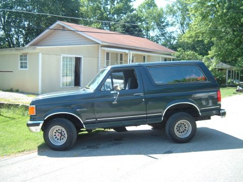 1988 Ford Bronco - Dark green Ford Bronco parked on a street in front of a house.