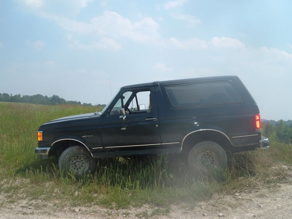 Black SUV with chrome trim on side, driving on a dirt path through tall grass