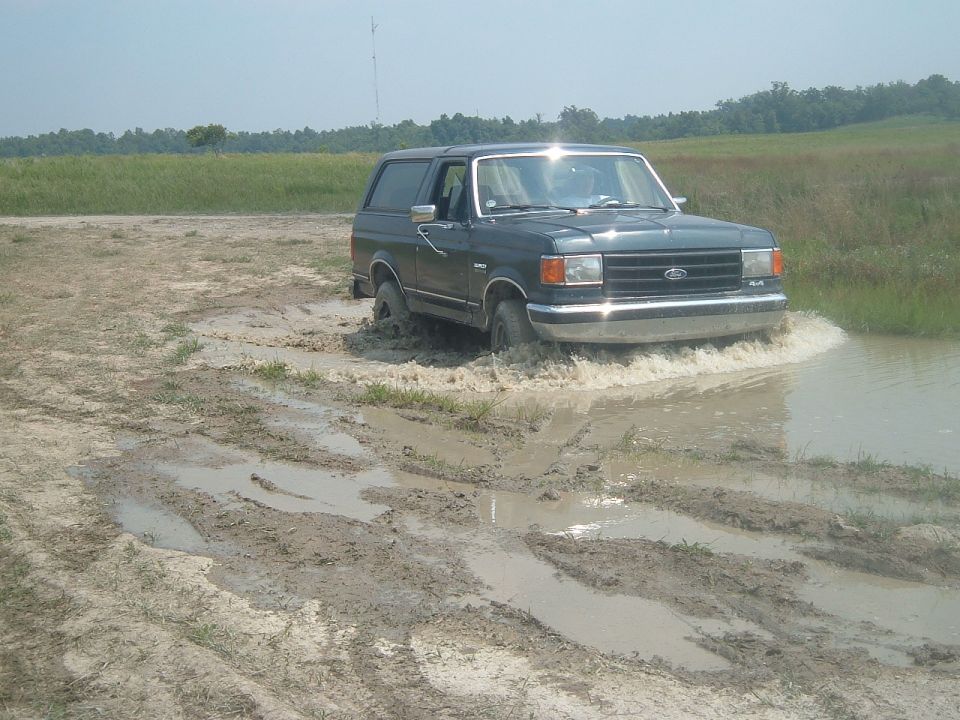 Dark green SUV splashing through mud, 1987 model year identified by body style