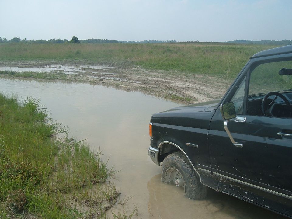dark SUV stuck in a muddy puddle, field in background