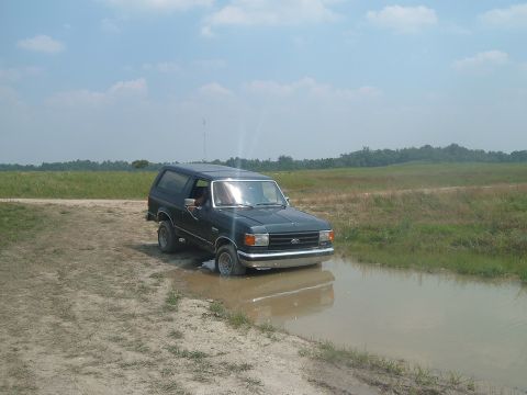1988 Ford Bronco - This SUV appears to be from the late 1980s, possibly a 1987 model, stuck in a muddy puddle off-road.