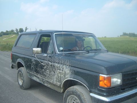 1988 Ford Bronco - This muddy SUV, likely a 1987 model, is shown from the front three-quarter view, ready for off-road adventure.