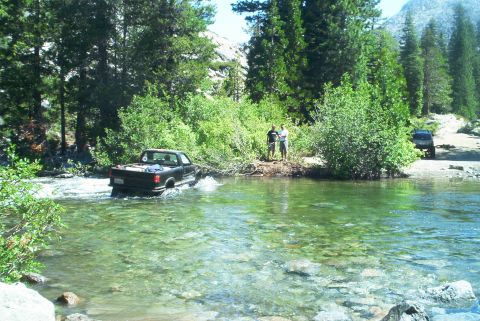 1966 Jeep CJ5 - A black pickup truck navigates a river crossing in a wooded, mountainous area.