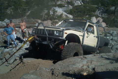 1966 Jeep CJ5 - A modified pickup truck is being winched through a challenging rocky off-road course.