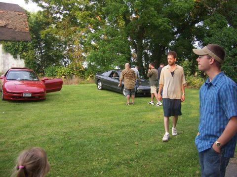 1996 Ford Probe - A gathering of people are seen around two cars parked on a lawn on a sunny day.