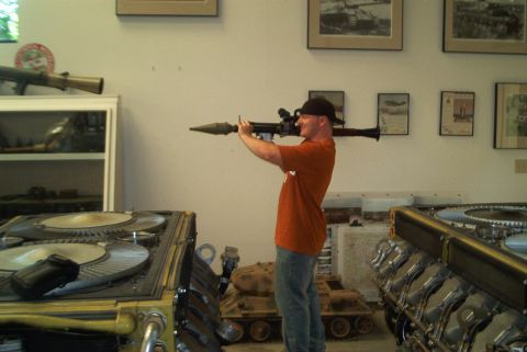 1966 Jeep CJ5 - A man poses with a rocket launcher in a room filled with military models and engine components.